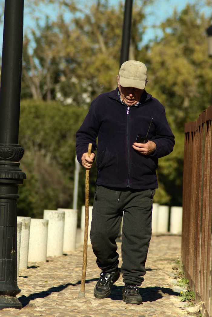 Senior man enjoys a sunny outdoor stroll using a cane and smartphone.
